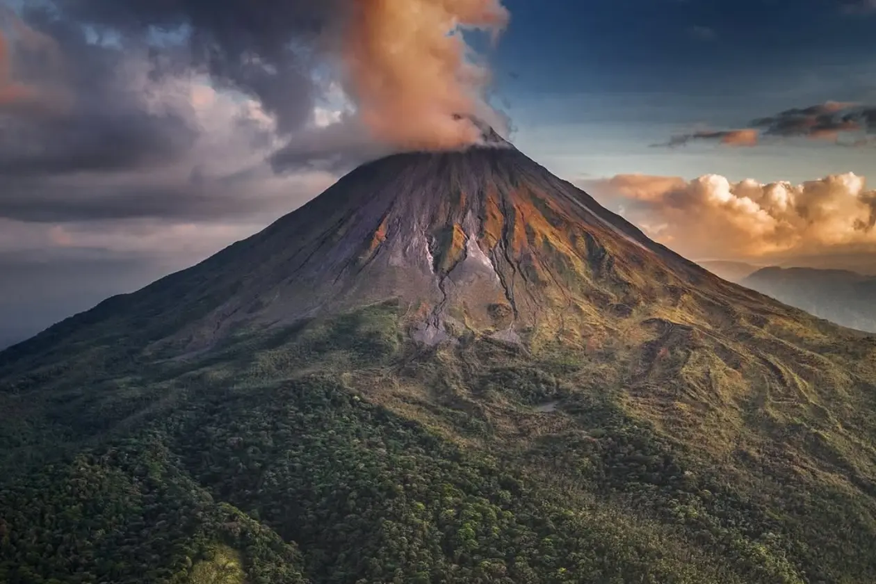 Volcán Arenal con una nube sobre la cumbre, iluminado por la luz cálida de la tarde sobre el bosque verde