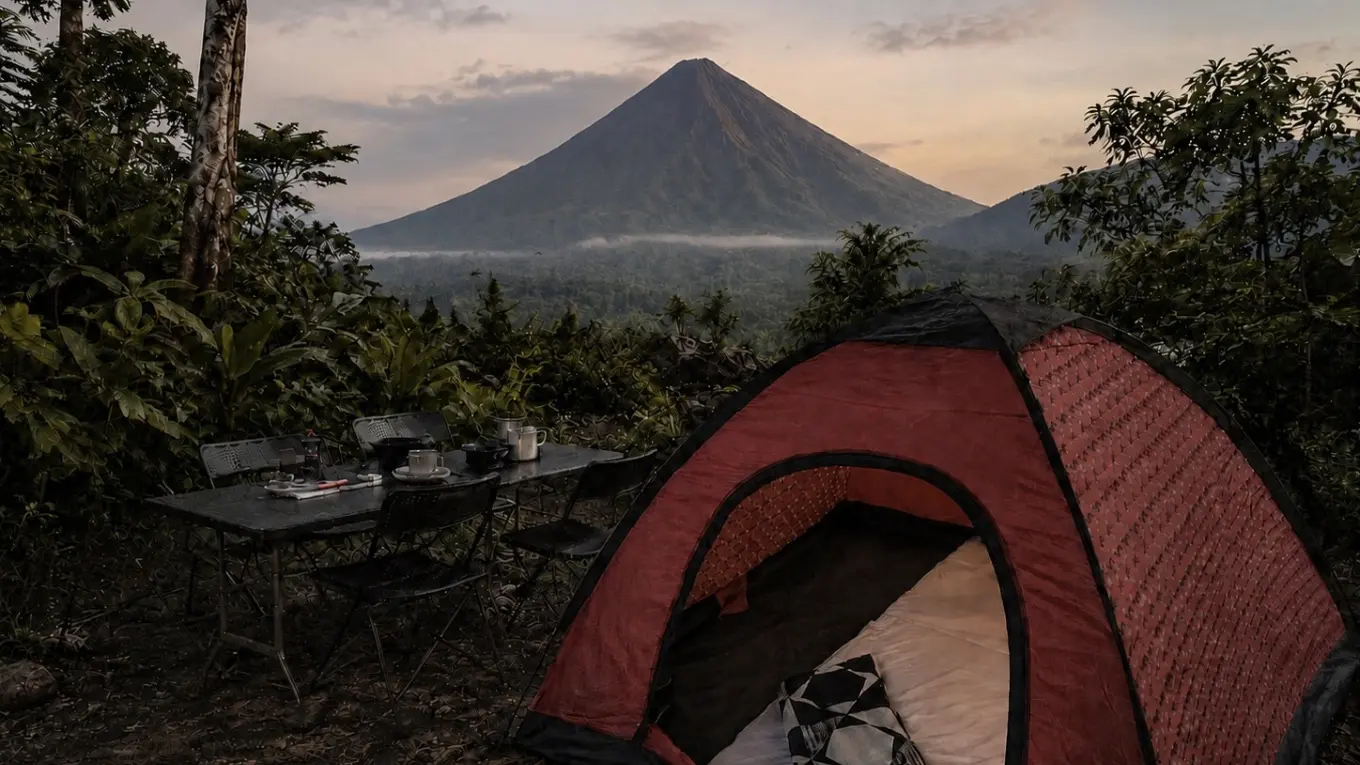 Red dome tent and a table set with mugs at dusk, with Arenal Volcano rising over the forest behind