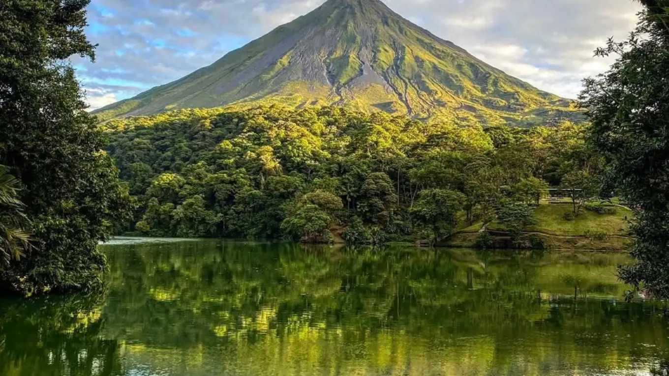 Forested slope and cone of Arenal Volcano reflected in a calm lake in warm morning light