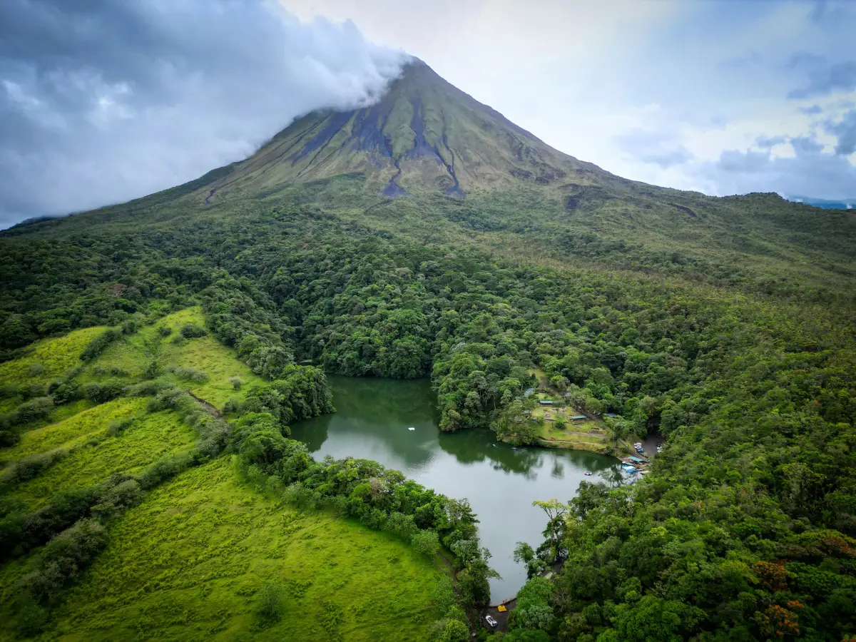Aerial view of Arenal Volcano above forest, green pastures and a small lagoon