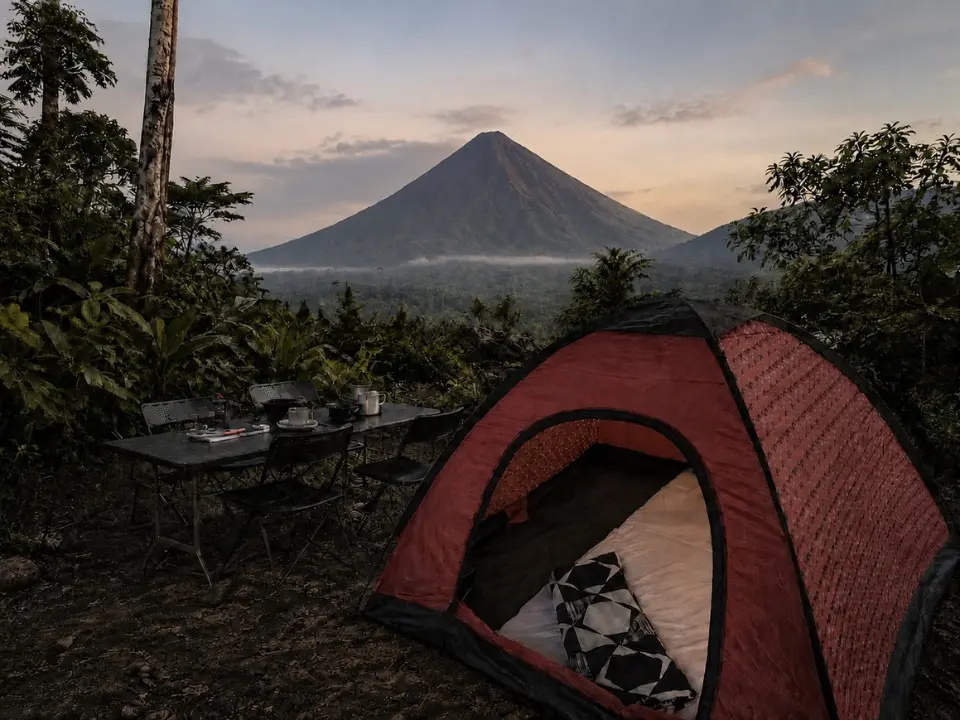 Carpa roja junto a una mesa en un claro del bosque, con un volcán que se alza al atardecer al fondo