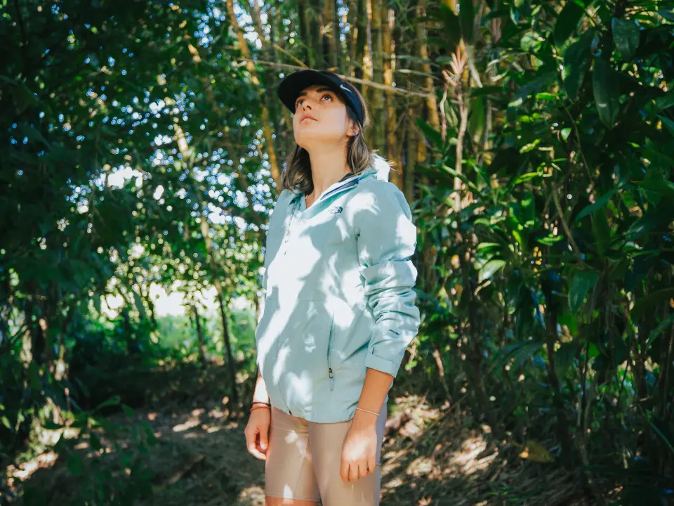 Person in a cap and light jacket looking up on a forest path among bamboo and leaves